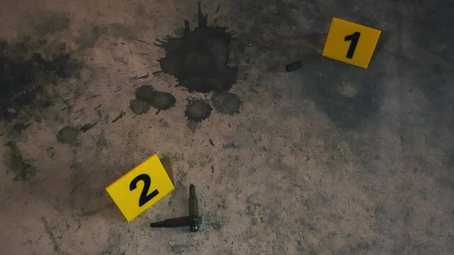High caliber bullets and a 9mm casing lying next to numbered yellow evidence markers on a dusty and stained concrete floor, suggesting a recent criminal act and forensic investigation