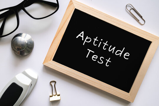 Aptitude Test text on black chalkboard with glasses and office supplies on white background, education and HR concept