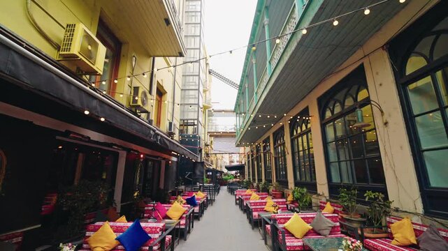 Brightly cushioned benches and tables line an empty narrow alley strung with light bulbs in central Tbilisi.