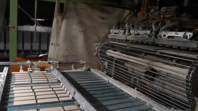Pneumatic pick and place unit hovers above rows of raw tiles on a factory roller conveyor