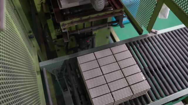 Automated stacker lowers onto a block of tan ceramic tiles behind a wire mesh safety guard