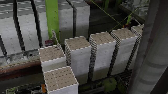 Tall stacks of unfired tiles are loaded onto kiln car platforms inside a ceramic tile factory
