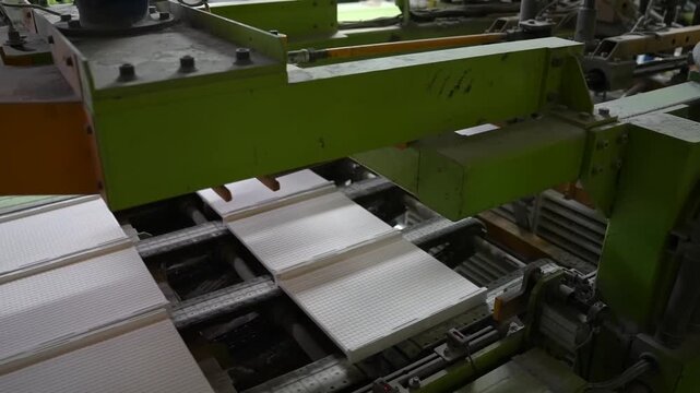 Green hydraulic press forms white ceramic tile sheets on an automated production line