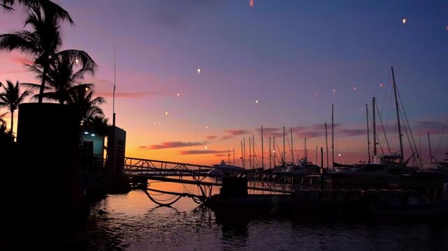 Sailboats rest in a marina beneath a colorful sunset sky. Palm trees and dock structures frame the calm waterfront creating a peaceful evening scene in Mexico