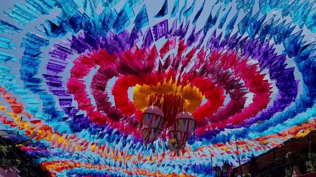 Colorful papel picado decorations form vibrant canopy over Mexican street with intricate patterns and festive colors. Traditional celebration atmosphere in Mexico.