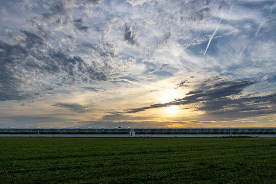 Dramatic Sunset Sky Over Large Agricultural Greenhouse Complex and Green Meadow