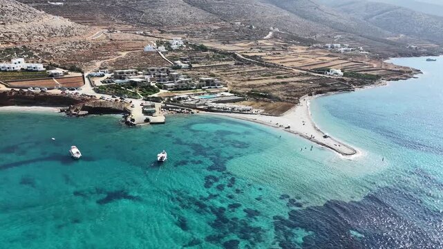 Aerial drone shot flying toward the sandy beach and gravel spit of Agios Pavlos across clear turquoise reef water off the north coast of Amorgos, Cyclades, Greece