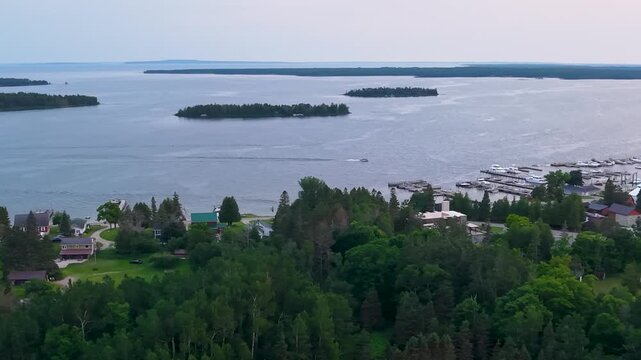 High drone view shows a wooded Hessel shoreline with homes and a marina below several islands across Lake Huron.