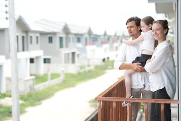 Fototapeta premium Caucasian family of three embracing enjoy the view of the growing suburb from their balcony standing on the terrace of a newly built suburban home, candid real moment