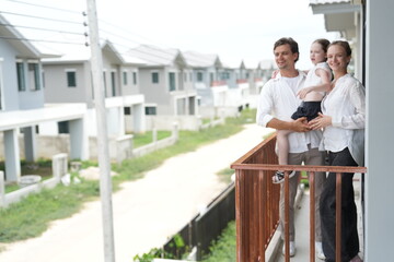 Fototapeta premium Happy young family with little daughter look out over the rows of new white houses from the railing on the upper balcony of their new home above the neighborhood in warm natural light