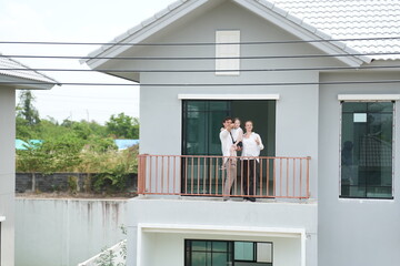 Fototapeta premium Happy young family with little daughter enjoy the view of the growing suburb from their balcony standing on the terrace of a newly built suburban home with copy space