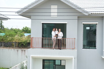 Fototapeta premium Young parents holding their child enjoy the view of the growing suburb from their balcony standing on the terrace of a newly built suburban home with copy space