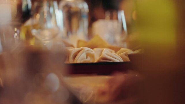 Steamed Georgian khinkali dumplings on a plate at a restaurant table, shot through soft foreground bokeh.