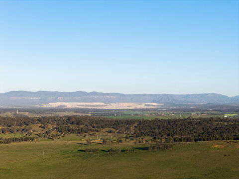 open cut coal mine scarring rural landscape in the Hunter valley seen on distant horizon