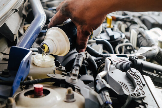 Mechanic hand servicing a car engine, adding brake fluid for maintenance and repair