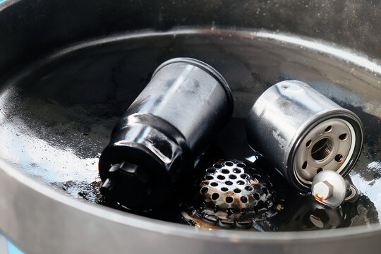Used oil filter and drain plug sitting in an oil drain pan after an oil change