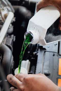 Mechanic adding green antifreeze liquid to a car engine during maintenance
