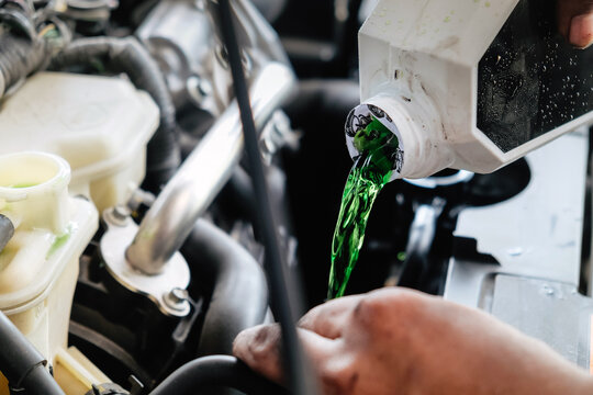 Mechanic adding green antifreeze liquid to a car engine during maintenance