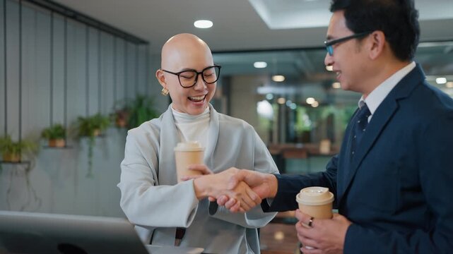 Two professionals shake hands in a modern office. They smile, showing mutual respect and trust. Coffee cups suggest a casual, collaborative meeting