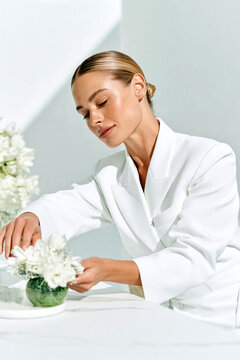 Elegant receptionist preparing a restrained floral arrangement at a reception desk before the workday, creating a welcoming festive atmosphere within a bright modern professional interior.