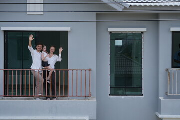 Obraz premium Caucasian family of three embracing greet the neighborhood from the balcony with their daughter on the balcony of their new house overlooking the residential estate, shallow depth of field