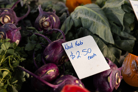 Fresh purple kohlrabi bulbs displayed at a market stall with handwritten sign &ldquo;Khol Rabi $2.50 each"