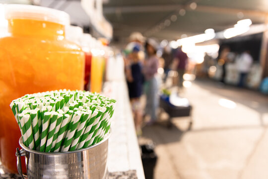 Metal container filled with green‑and‑white striped paper straws sits on a market counter