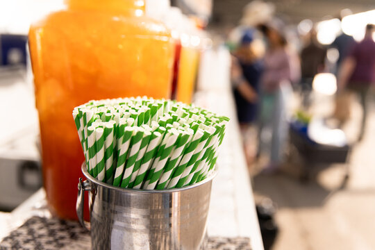 Metal container filled with green‑and‑white striped paper straws sits on a market counter
