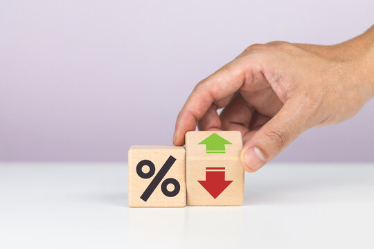 Hand placing a wooden block with green up and red down arrows next to a percentage sign block, illustrating interest rate reduction and financial adjustment