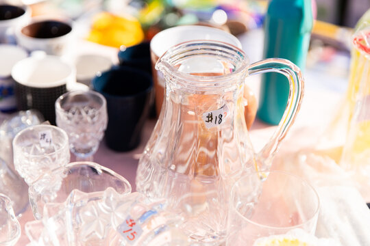 Assorted glassware and ceramic cups displayed on a market table with clear glass jug marked &ldquo;$18&rdquo;