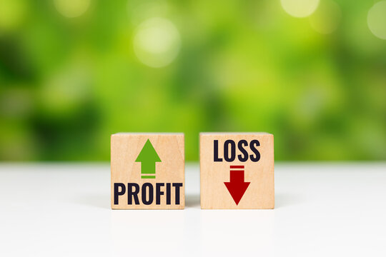 Wooden cube blocks displaying PROFIT with green arrow up and LOSS with red arrow down on white table, symbolizing financial outcome and stock market trend