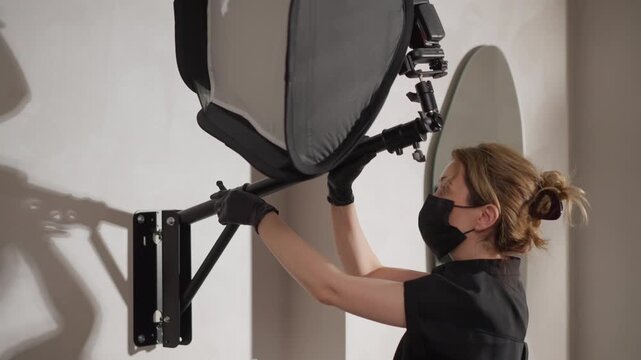 Close up of woman adjusting studio lighting equipment in soft indoor light. Woman wears black gloves and attire focusing on positioning large gray reflector attached to adjustable arm