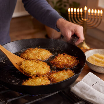 Potato latkes frying beside a Hanukkah menorah