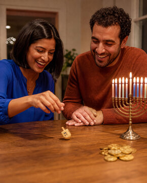 Two adults playing dreidel beside a lit Hanukkah menorah