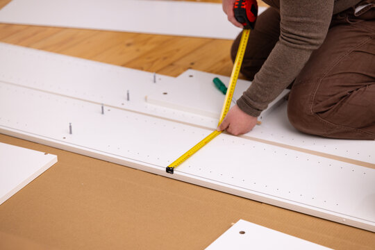 Adult woman kneeling on a polished wooden floor measuring a white furniture panel