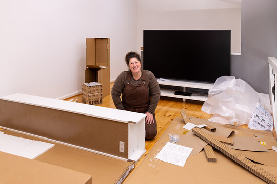 Adult woman kneeling on a polished wooden floor, assembling flat‑pack furniture