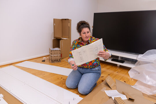 Woman reading flat-pack furniture assembly instructions while kneeling among white panels
