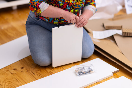 Close up of woman kneeling on wooden floor inserting wooden dowels to assemble flatpack furniture