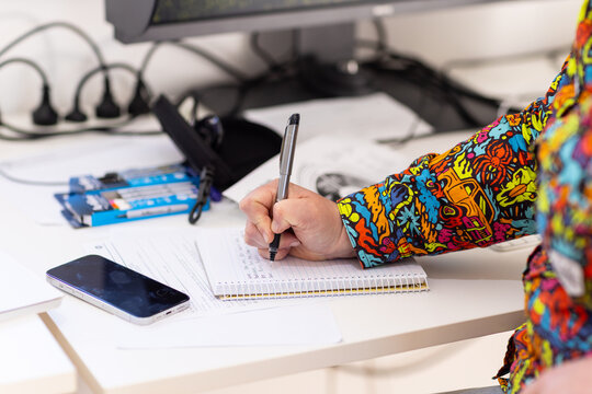 Close-up of woman handwriting notes in a spiral notebook at a modern office desk with smartphone