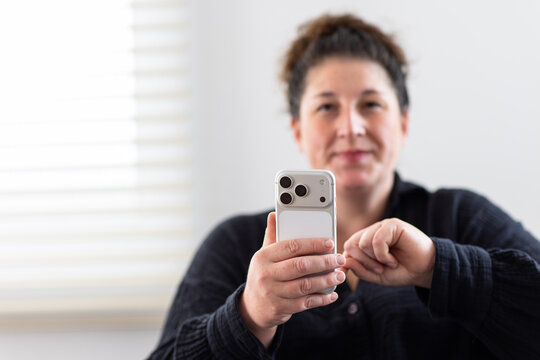 Woman holding smart phone facing front with blurred background indoors