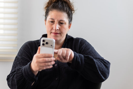 Woman in black shirt holding smart phone and tapping screen with finger indoors
