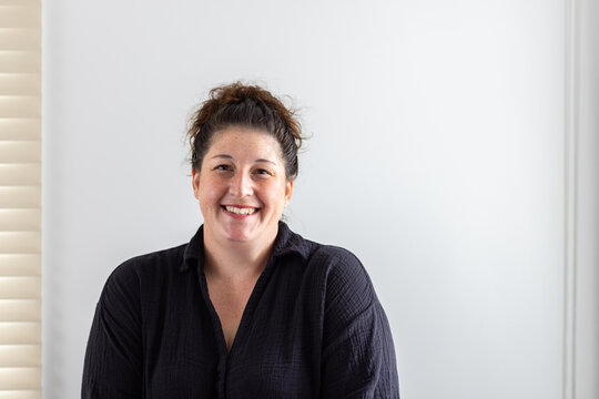 Portrait of smiling woman in black shirt against neutral white wall background