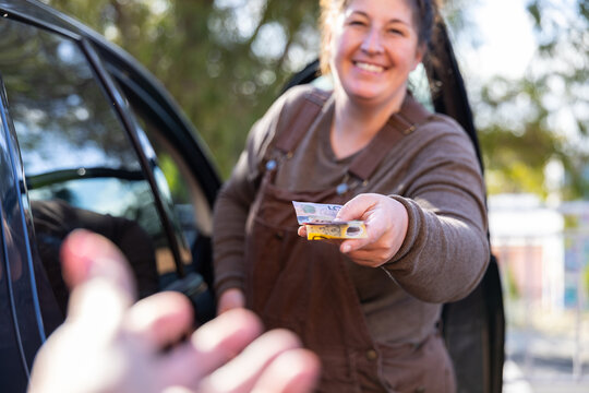 Woman wearing overalls handing over cash bank notes to person standing near car
