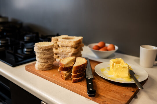 Bread and butter sit on a wooden board with eggs nearby in a kitchen preparing for breakfast