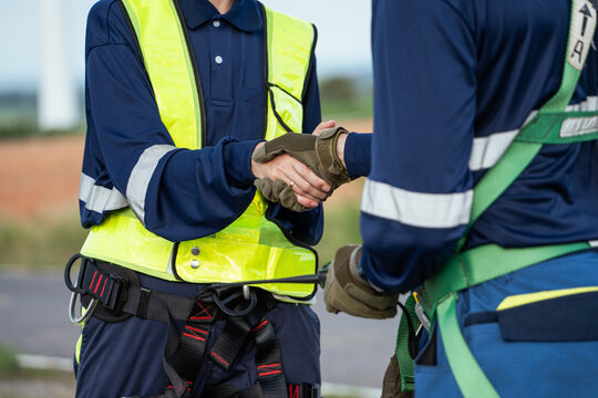 A team of technicians wearing safety harnesses shake hands outdoors, sealing an agreement on a wind farm project and conveying a sense of professional cooperation and trust.