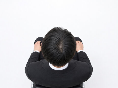 白背景で体育座りをするスーツ姿の男性の頭頂部
