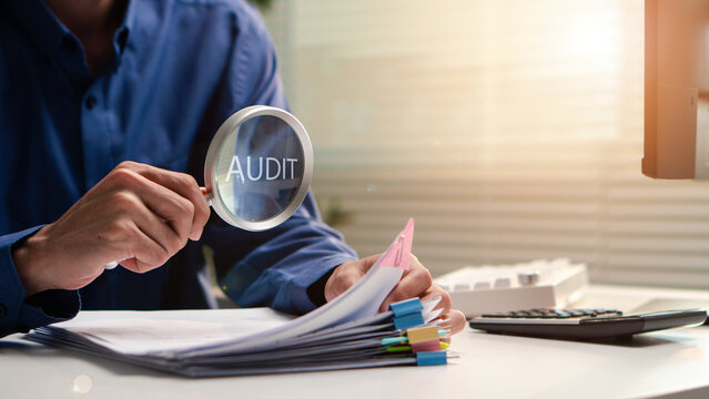 Auditor inspects business documents with a magnifying glass in an office. Concept of compliance, accounting review, financial control, verification, risk management, and corporate audit.