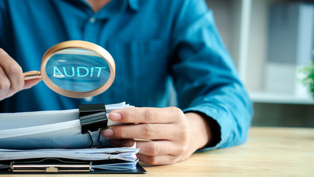 Auditor inspects business documents with a magnifying glass in an office. Concept of compliance, accounting review, financial control, verification, risk management, and corporate audit.