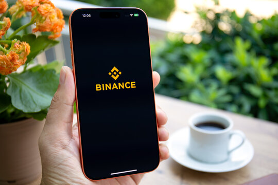 Mans hand holding phone Apple iPhone 17 Pro Max Cosmic Orange cafe displaying application cryptocurrency exchange Binance on screen smartphone