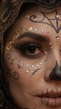 El Dia de Muertos Day of the Dead catrina makeup on a young female face, showing intricate sugar skull cosmetics with gold leaf accents, rhinestone gems and a black lace veil.